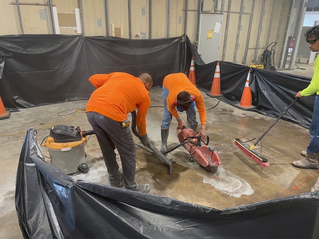 Crew saw-cutting a shop floor inside plastic containment.