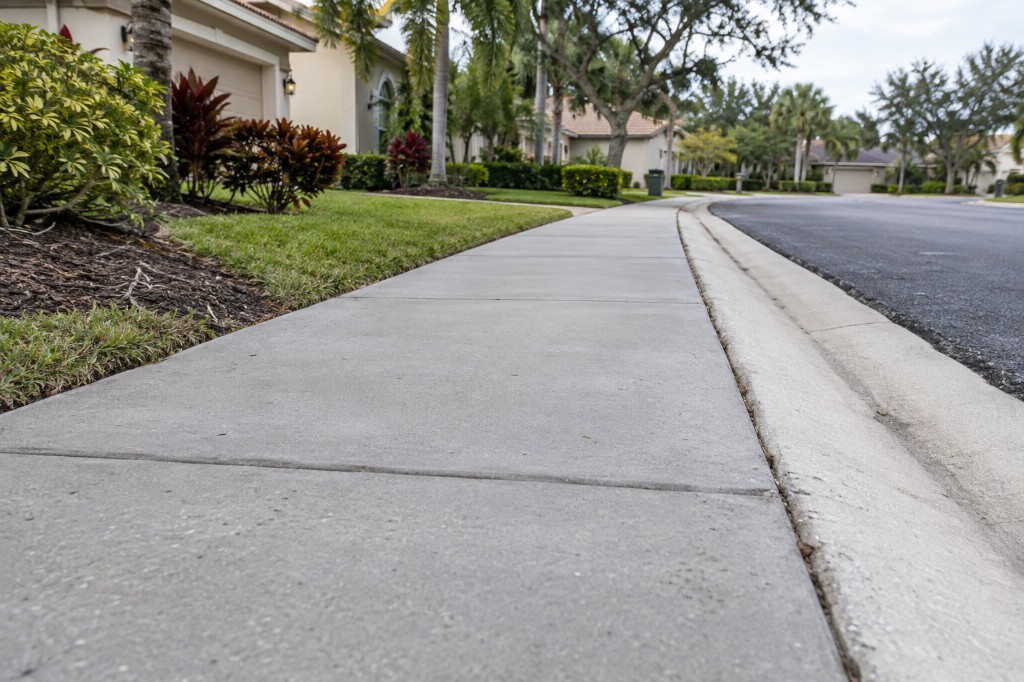A community sidewalk running beside a curb and a landscaped front yard.