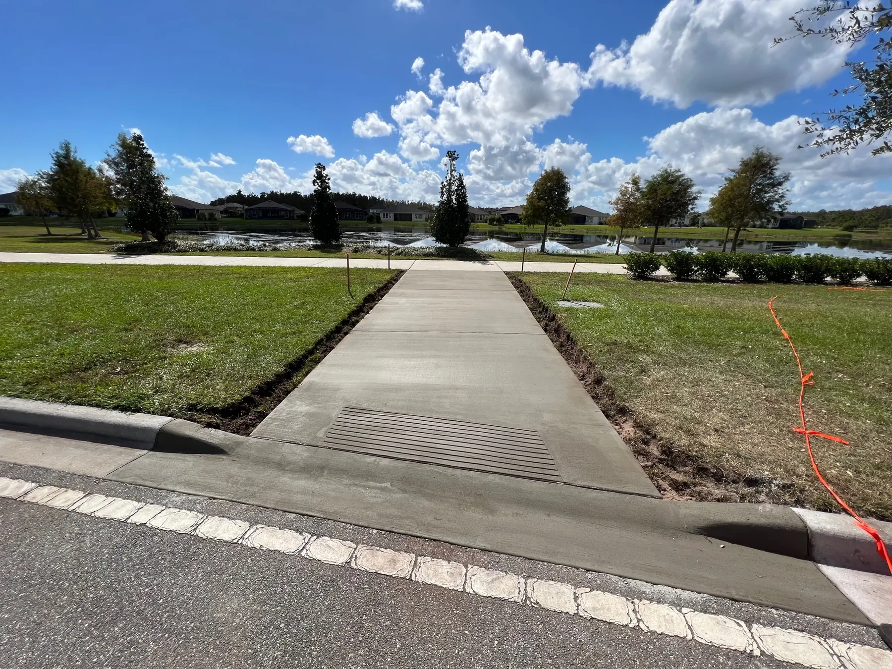 New sidewalk poured to the curb at a community street, with a drain grate set in the concrete.