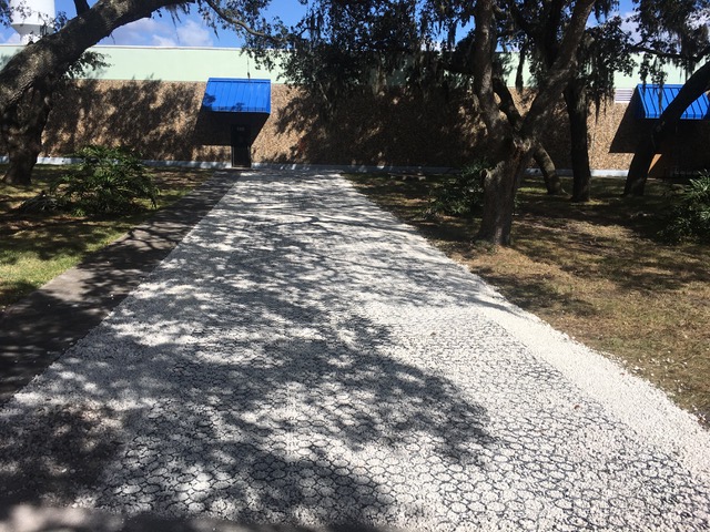 An exposed-aggregate drive leading to a community building, shaded by oaks.