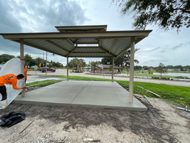 A new concrete slab under a community shade structure, with the crew still on site.