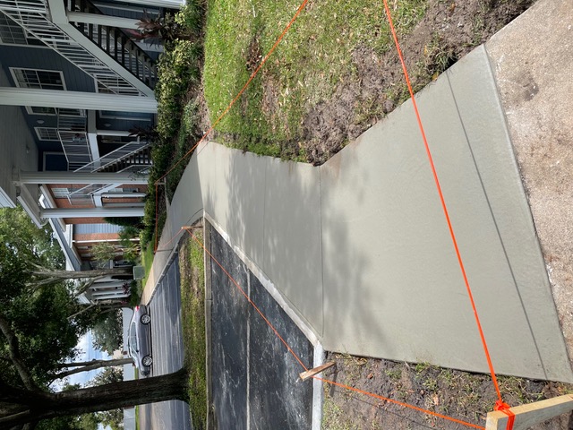 New concrete sidewalk along an apartment building, roped off with orange string.