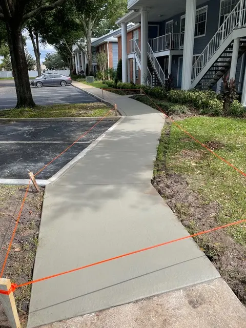 New concrete sidewalk along an apartment building, roped off with orange string.